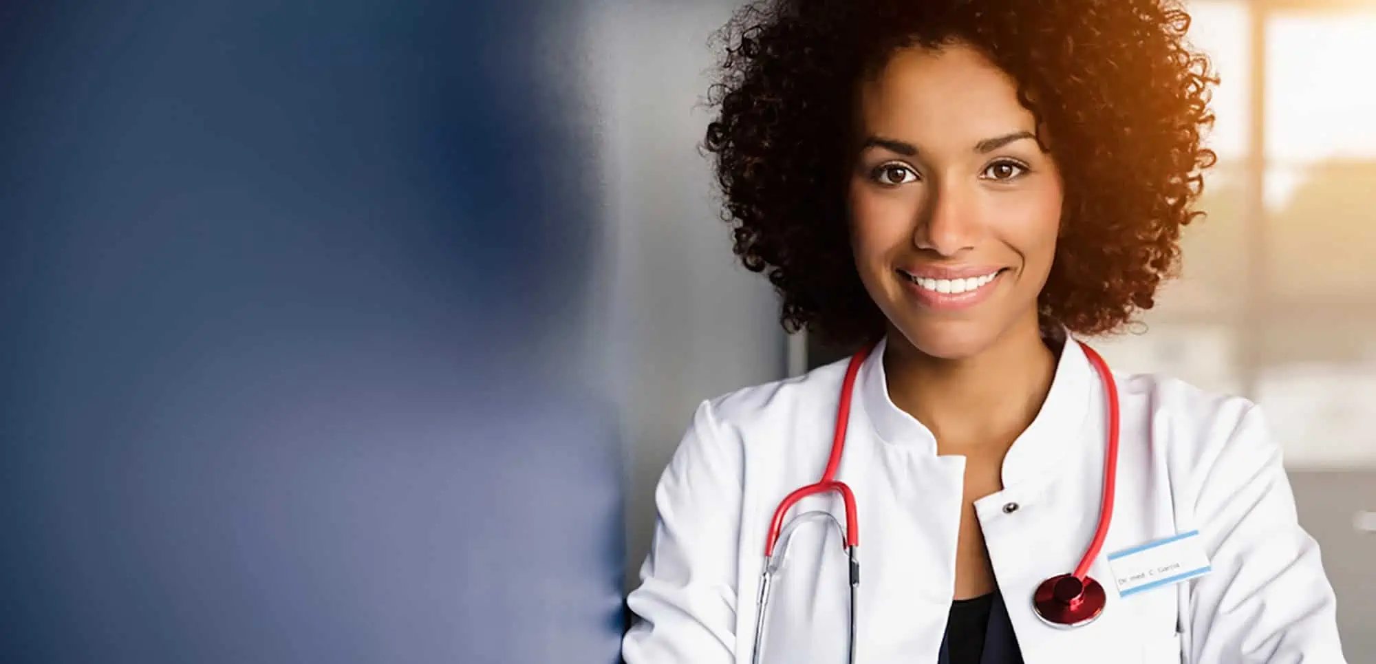 A young Black dermatologist smiles at the camera.